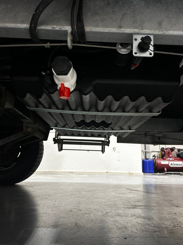 Underneath view of vehicle showing black corrugated mud flap with red light mounted on frame