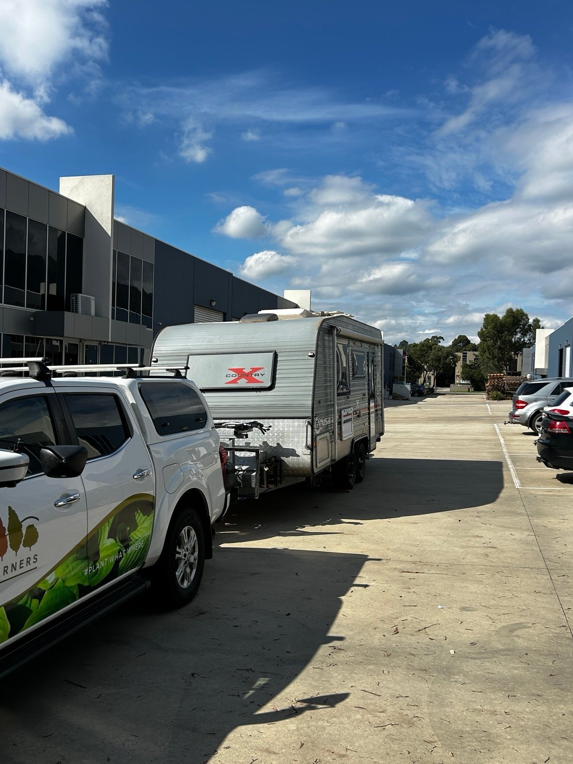 White travel trailer parked next to white pickup truck in a commercial lot under blue sky with clouds