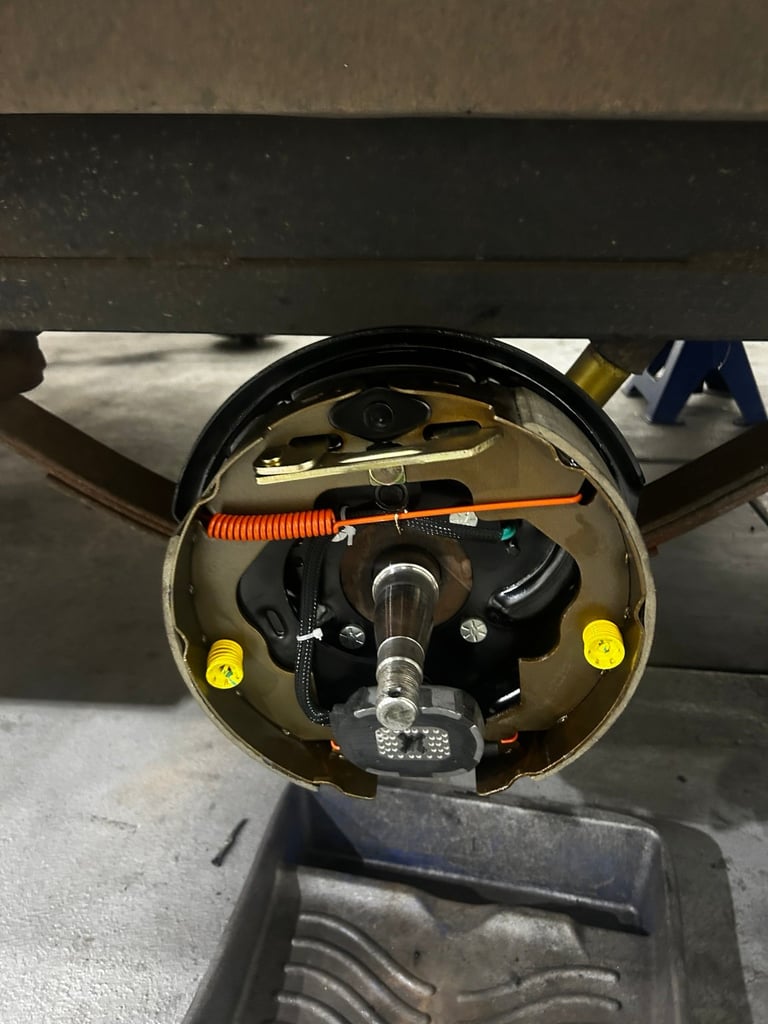 Interior view of a vehicles rear axle assembly showing brake components, wiring, and yellow adjustment features mounted on metal housing