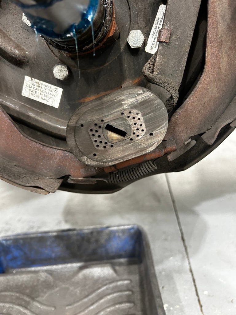 Close-up of a worn industrial pump or motor component with metal housing, hexagonal bolts, and a perforated metal disc in the center