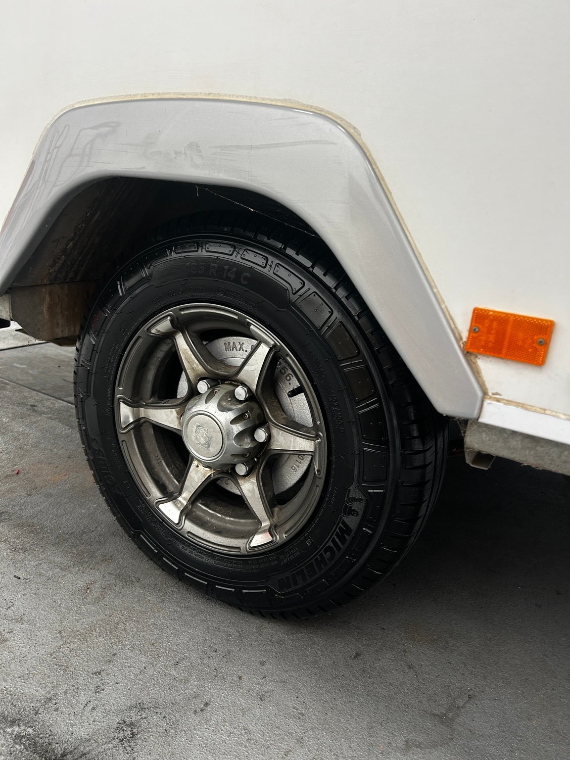 Close-up of a vehicles wheel and tire with white fender, silver alloy rim, and orange reflector visible