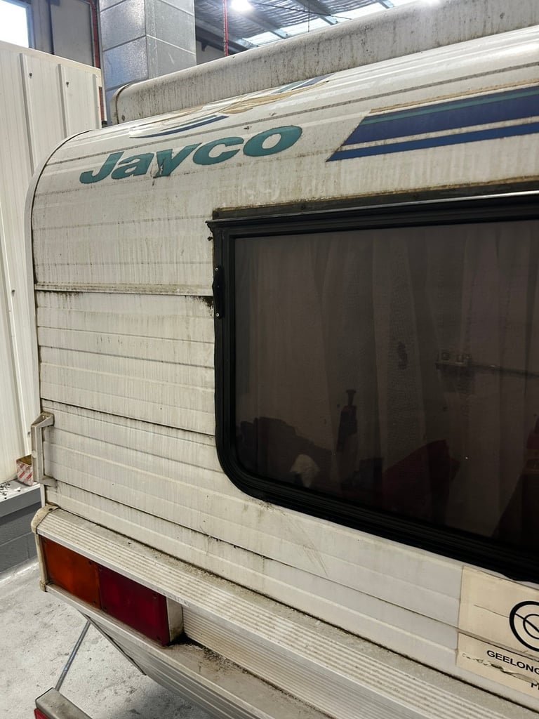 Jayco white travel trailer with teal and blue stripe and dark window, parked indoors