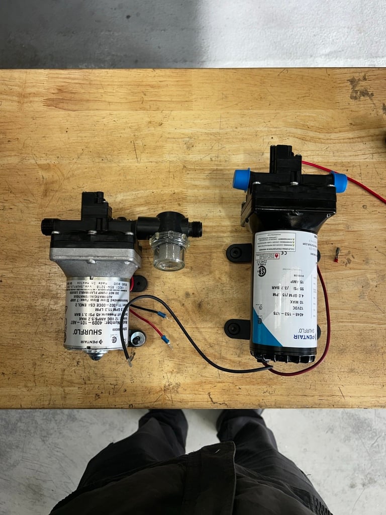 Two small electric water pumps with black housings and color-coded connectors displayed on a wooden surface