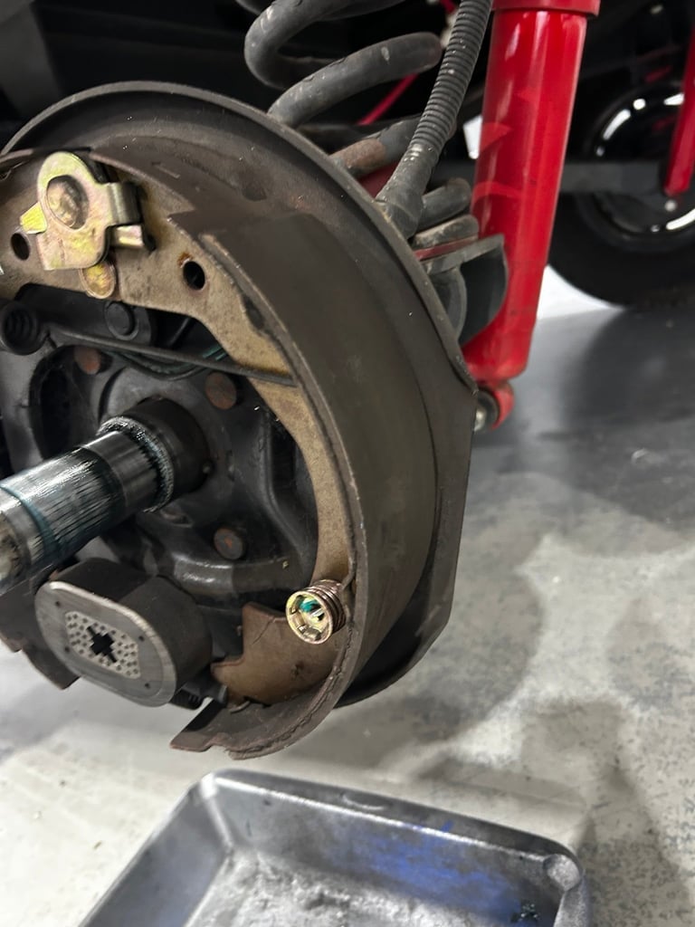 Close-up of a vehicle brake disc and caliper being serviced, with red brake components and a technicians hands working on the assembly