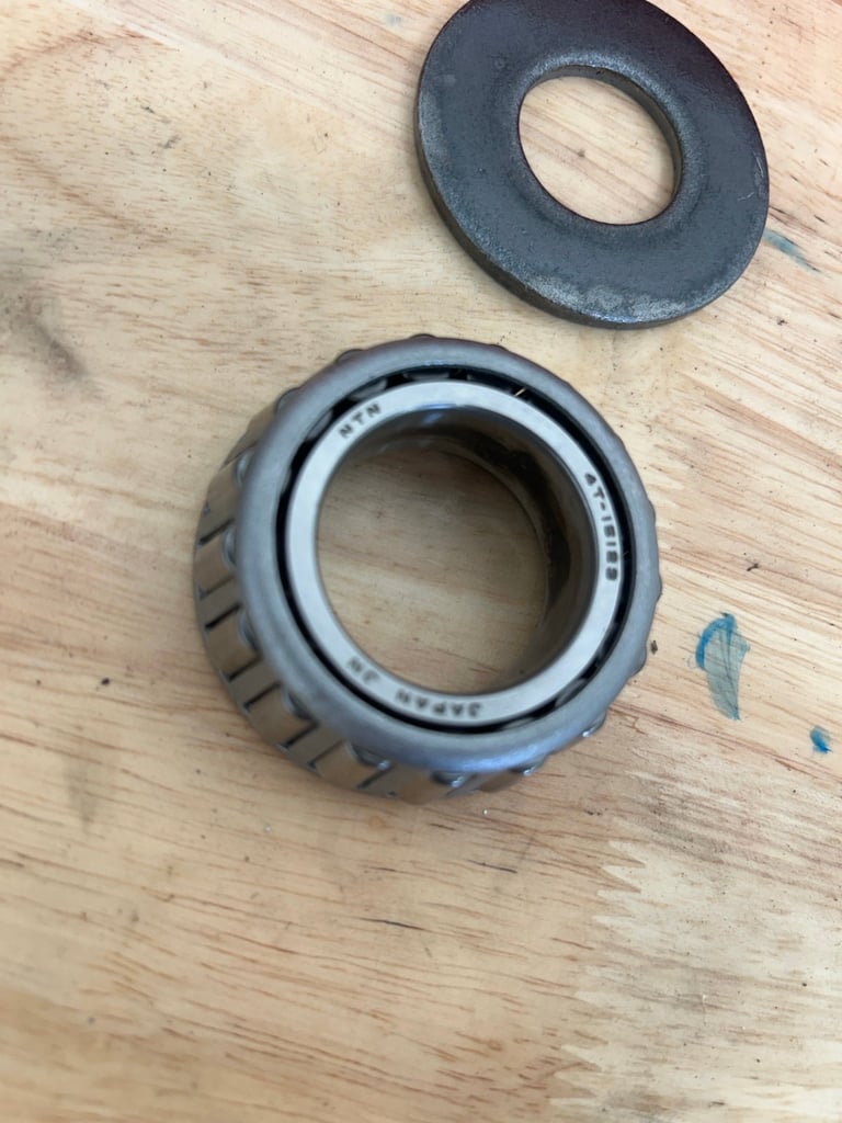 Disassembled tapered roller bearing with cone and race on wooden surface