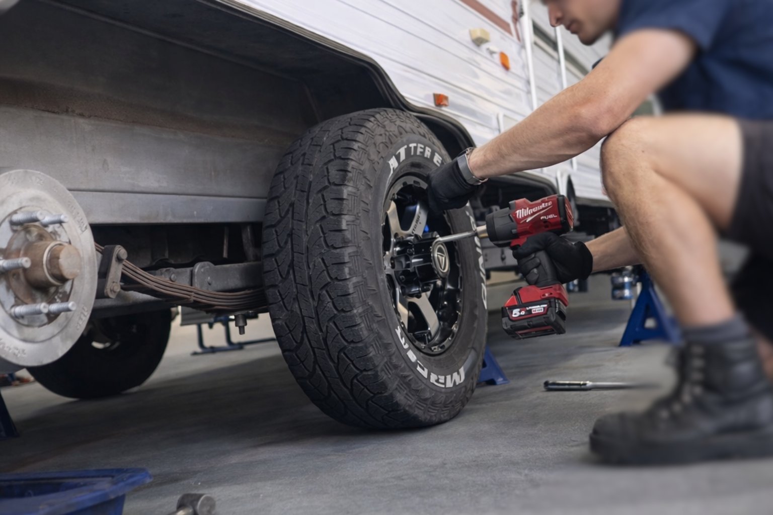 Mechanic using a power tool to work on a trucks tire during maintenance, with the vehicle lifted on a blue jack