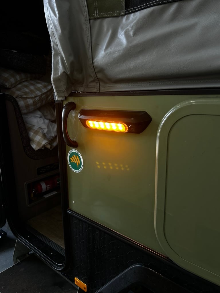 Illuminated amber side marker light on the fender of a vintage olive-green Jeep in a garage setting