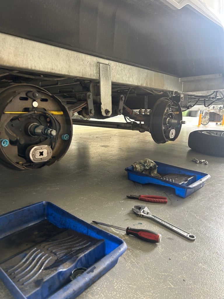 Vehicle undercarriage with exposed steering wheel and axle during maintenance, with blue tool trays and tools on concrete floor