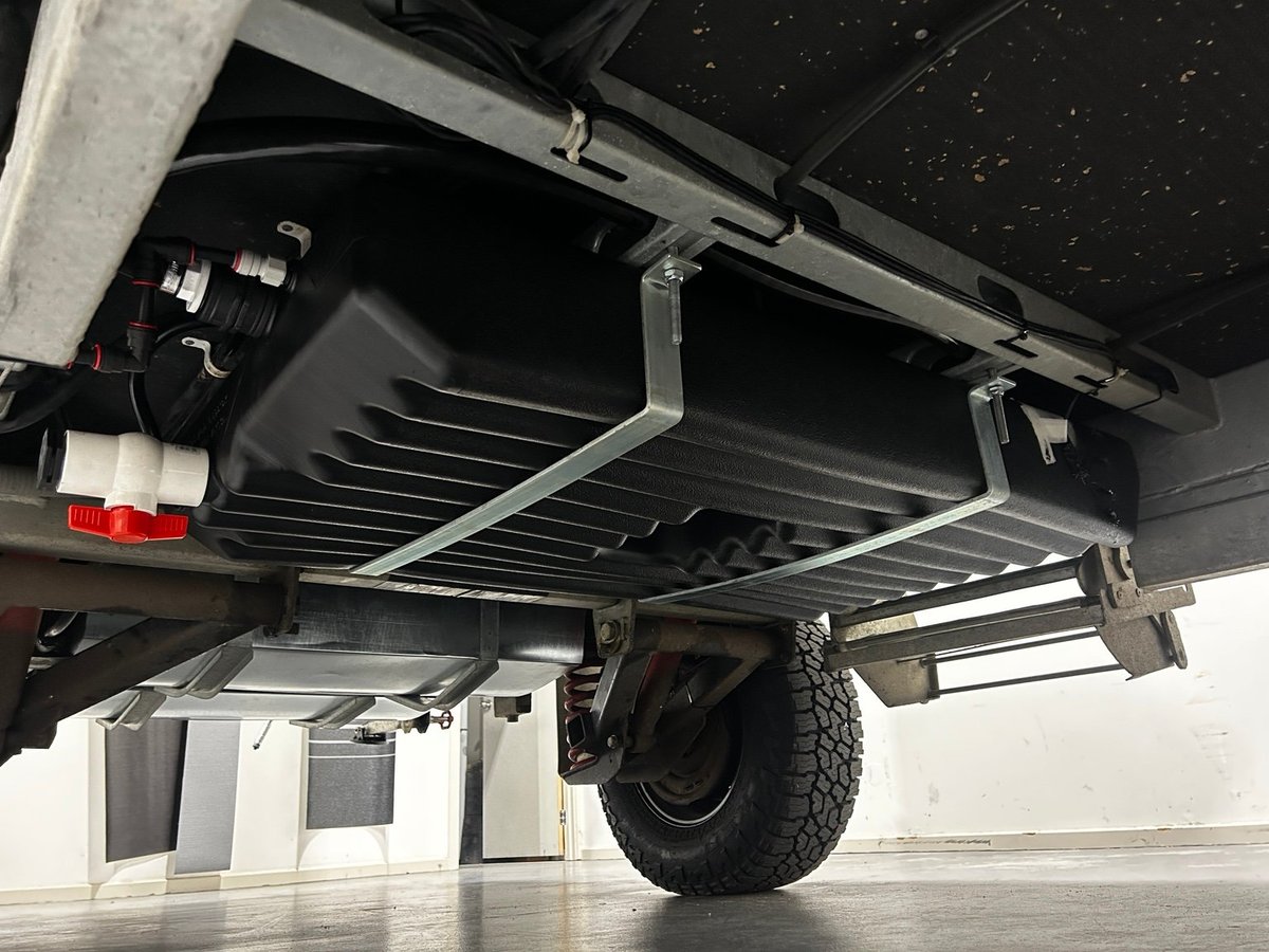 Underside of pickup truck showing reinforced frame, suspension components, and tire mounted on concrete surface