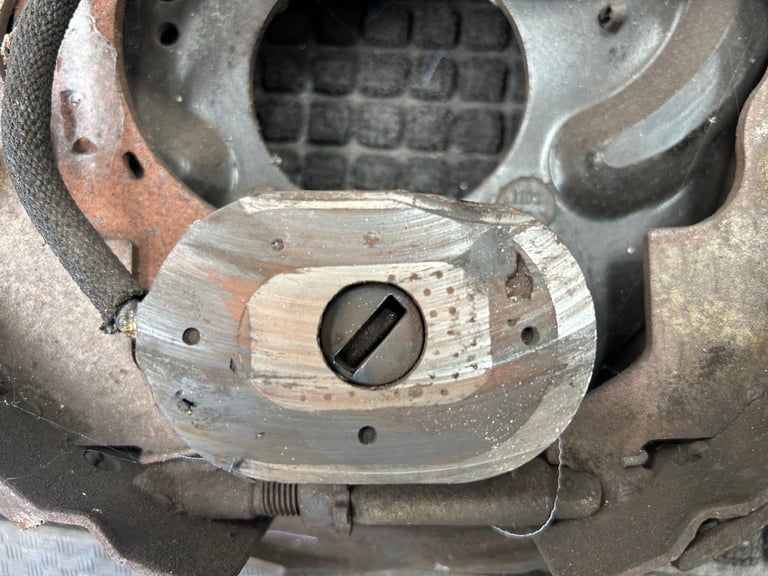 Close-up of disassembled engine component showing worn metal parts with mounting holes and central circular opening