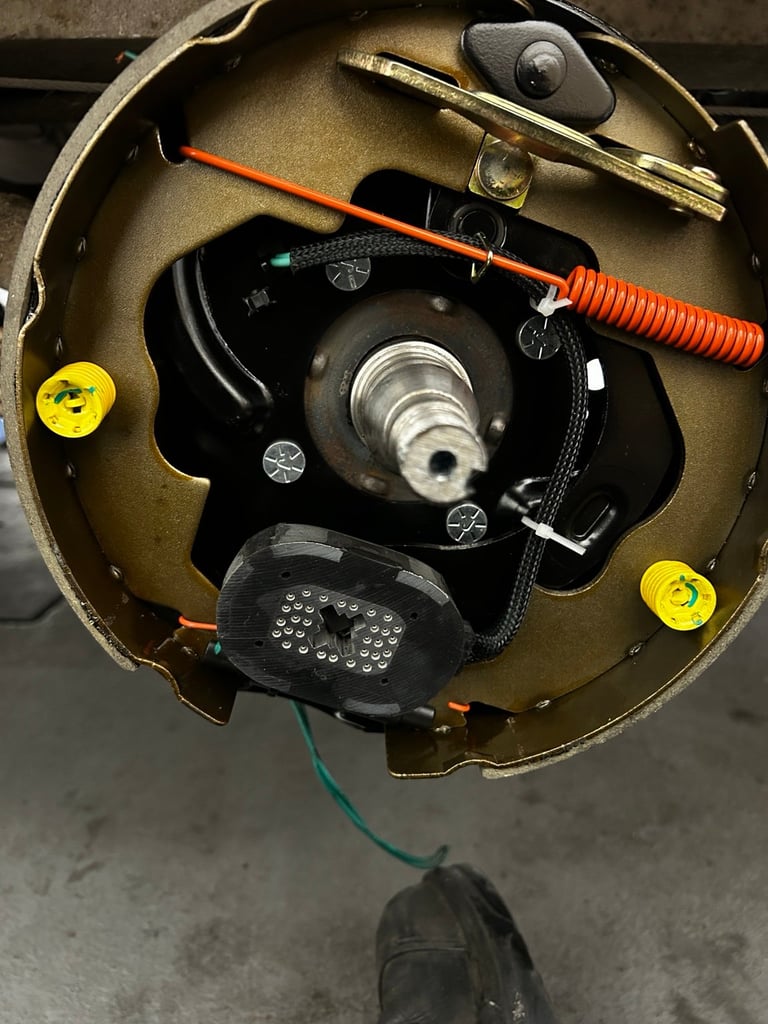 Overhead view of a car brake assembly showing the drum, springs, and hardware components with an orange adjustment tool