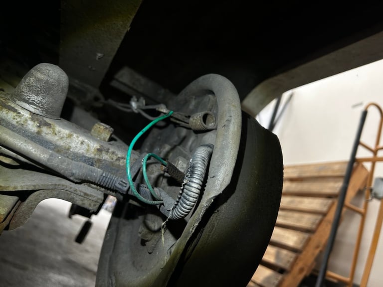 Close-up of a vehicles disc brake assembly with green wiring and metal components visible underneath a car