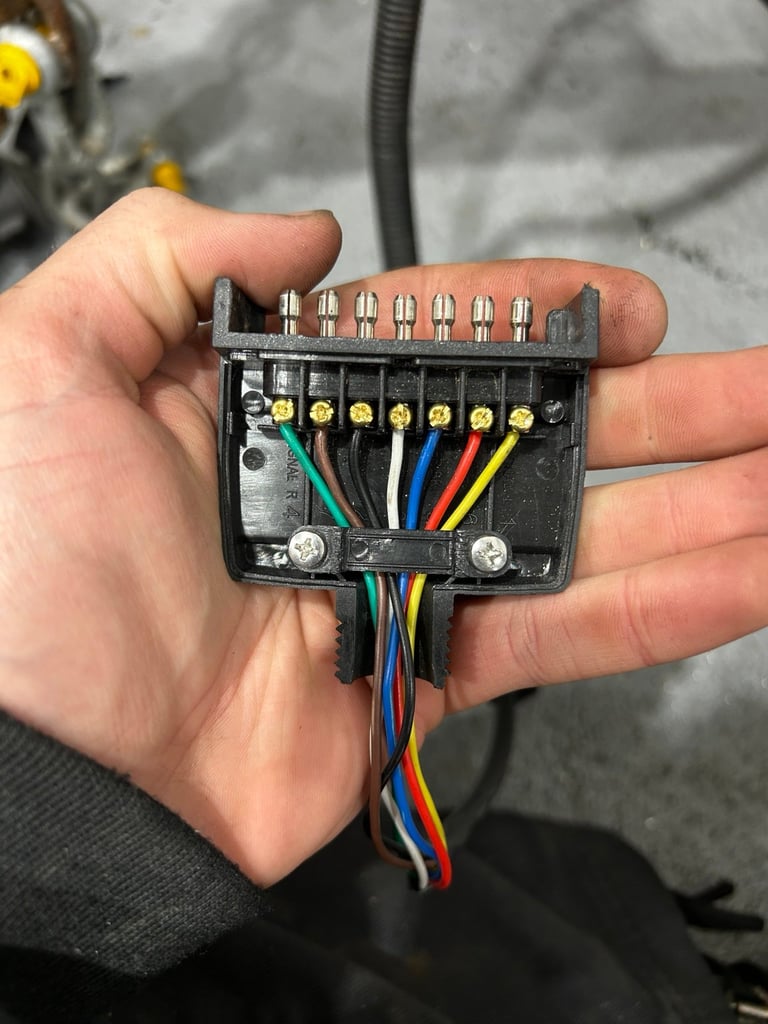 Hand holding a black electrical terminal block with seven colored wires connected to brass terminals