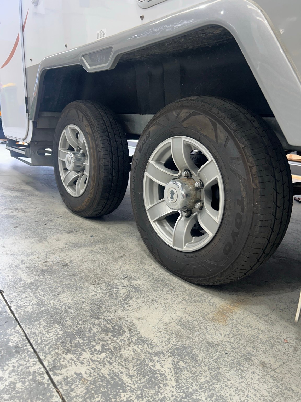 Two large tires with silver alloy wheels on a white pickup truck parked in a garage