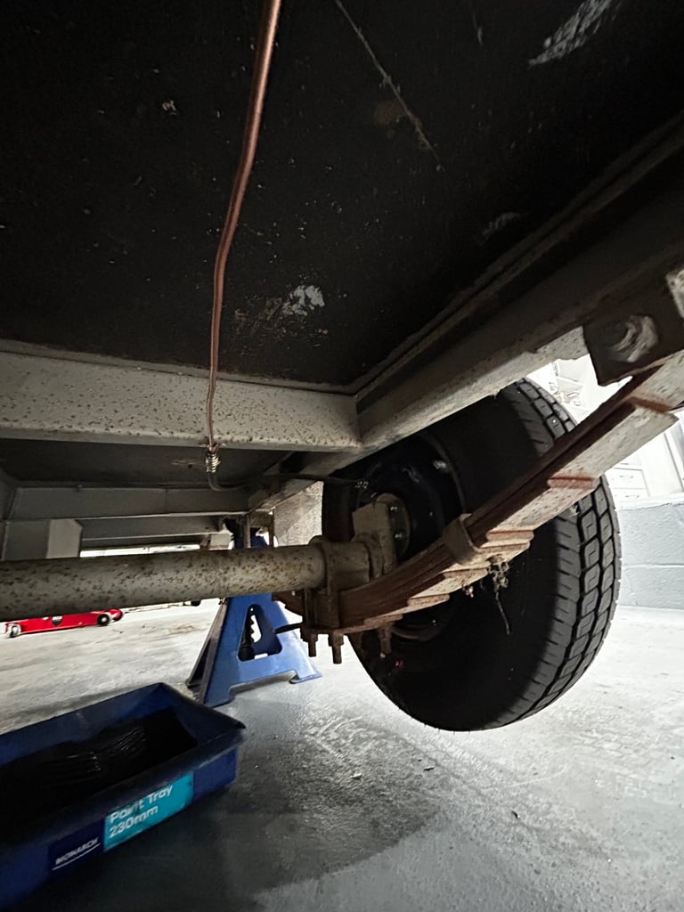 Underside of vehicle showing axle, suspension, and tire with blue jack on concrete floor in garage