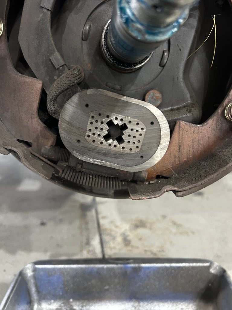 Close-up of a worn brake pad with perforated metal backing plate showing wear damage and rust, mounted in vehicle brake assembly