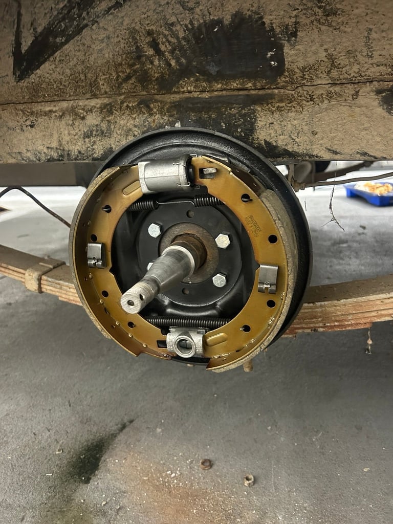 Exposed drum brake assembly showing brass backing plate, black components, and central axle shaft on vehicle wheel hub