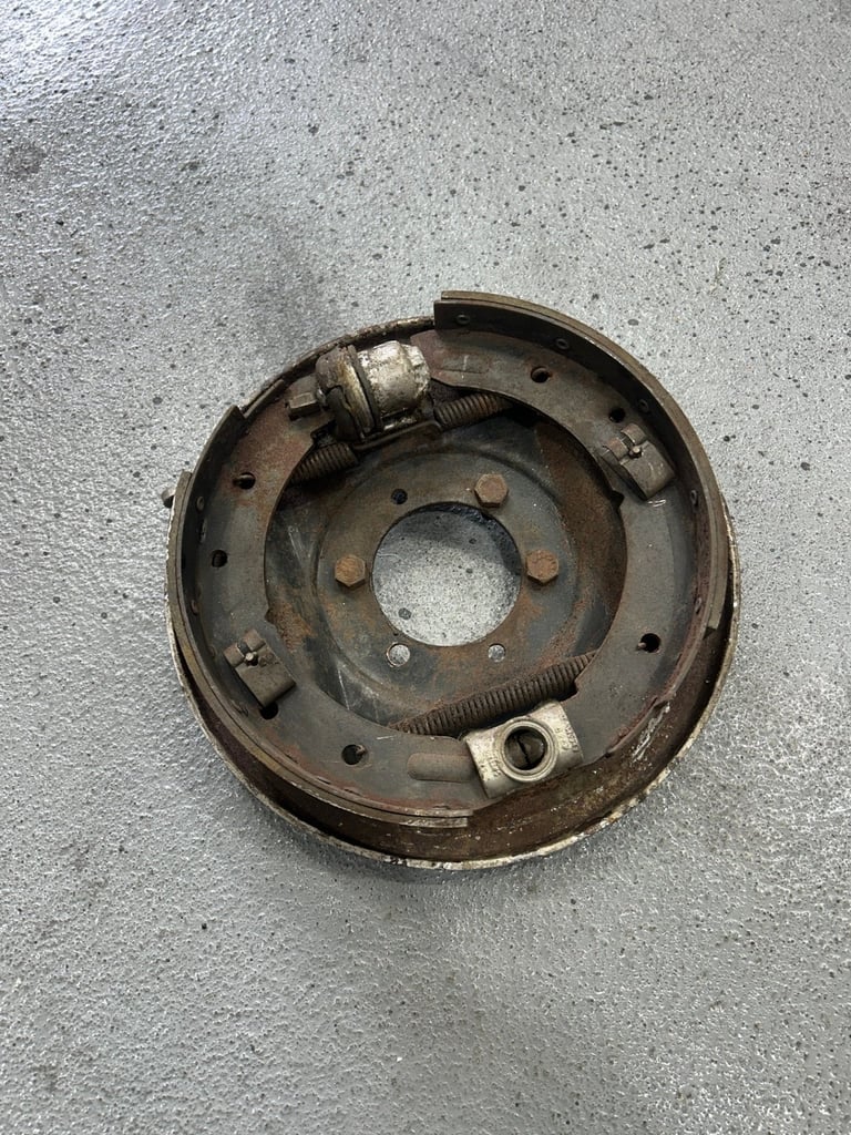 Rusty brake drum assembly with springs and bolts on concrete surface