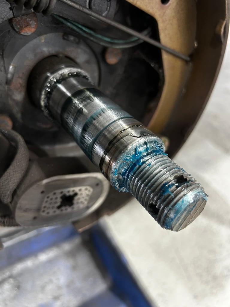 Close-up of a threaded metal stud or bolt with blue PTFE tape wrapped around it, mounted on a mechanical component with brake pads visible