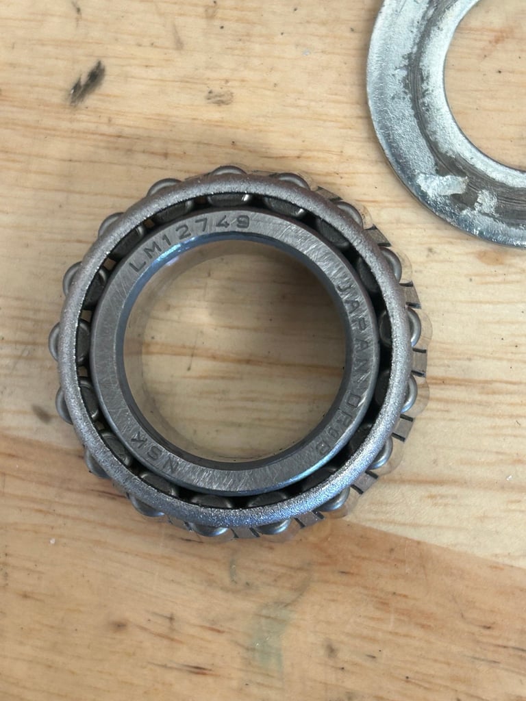 Metal tapered roller bearing with part number LM67048 on wooden surface