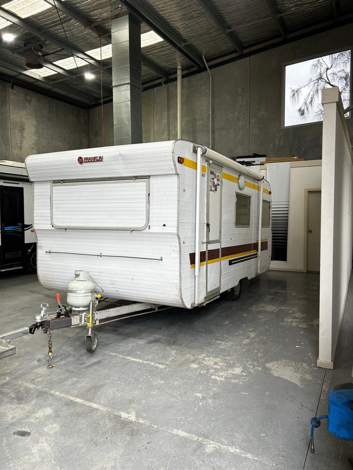 White and yellow travel trailer parked in industrial garage with concrete floor and metal support columns