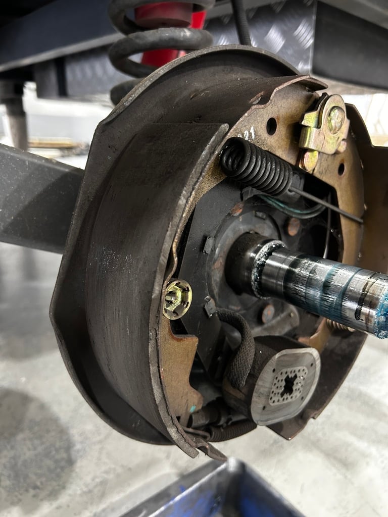 Disassembled vehicle drum brake showing internal components including spring, adjuster, and wheel cylinder