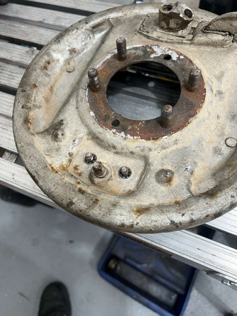 Close-up of a corroded metal brake drum with central opening and bolt holes, showing rust and wear