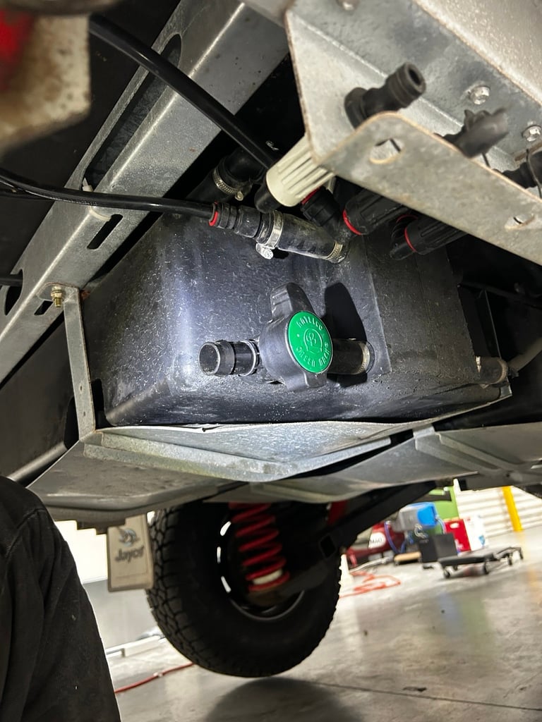 Close-up of vehicle electrical connection panel with green button, black cable, and metal mounting brackets