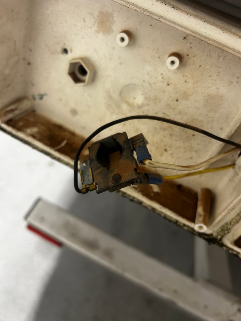 Interior view of electrical outlet box with brass switch mechanism and black wiring attached to cream-colored plastic housing