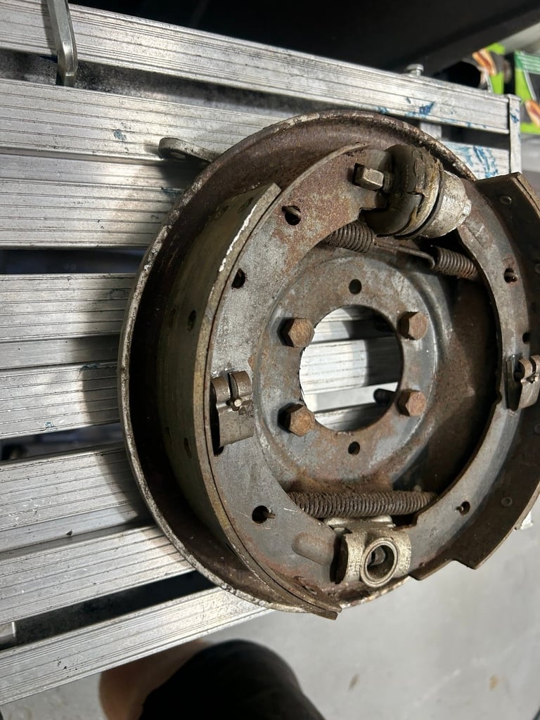 Rusty brake drum assembly with worn metal surface, bolts, and internal components visible on concrete surface