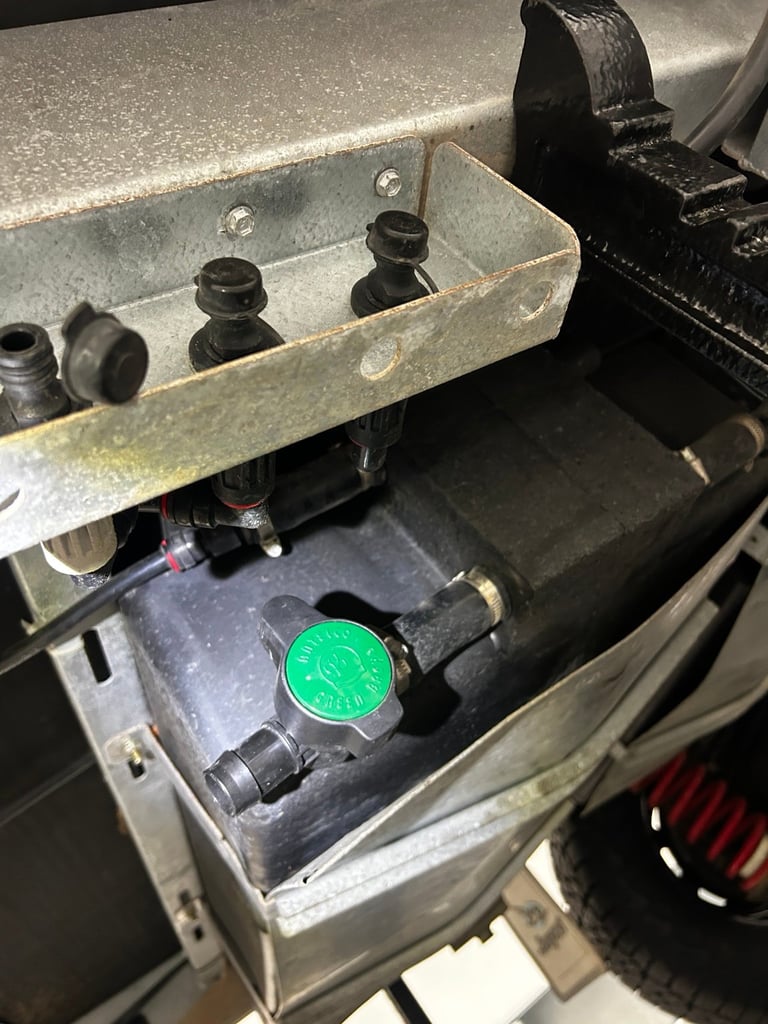 Close-up of an open car engine compartment showing a green battery cap and various engine components in a metal container