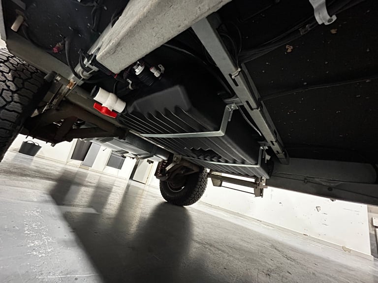 Underside view of a vehicle showing the chassis, wheel, and mechanical components with concrete structure above