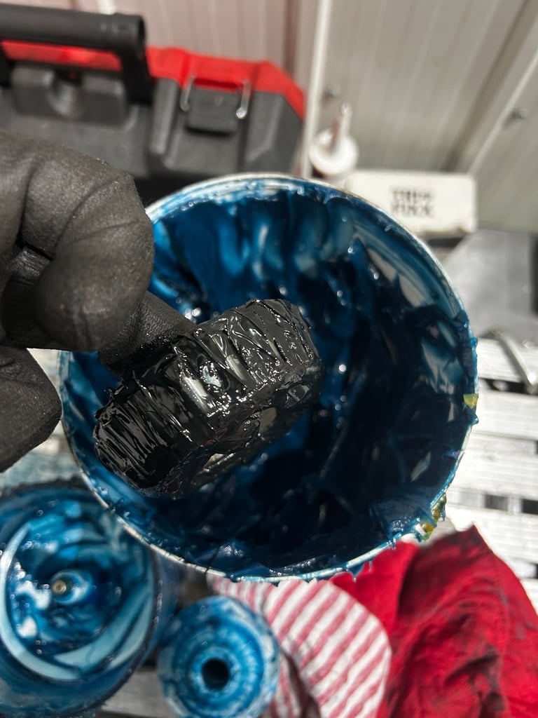 Hand holding a blue bucket containing black graphite or charcoal material in an industrial workshop setting