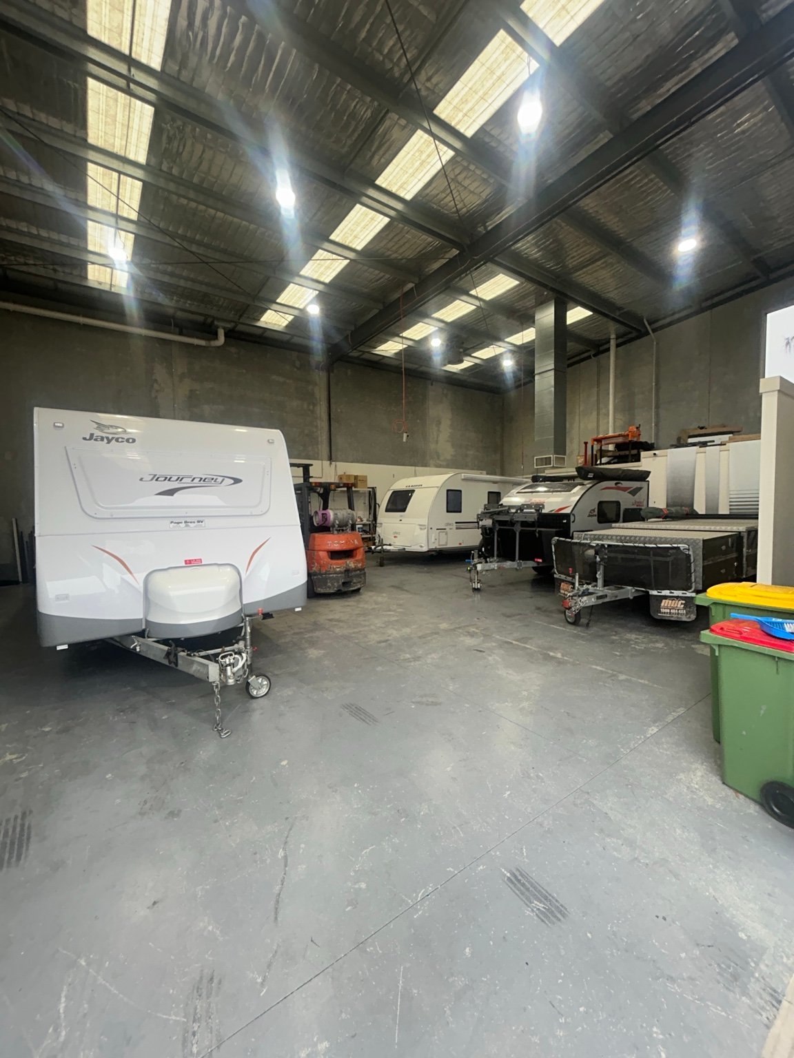 Indoor storage facility with multiple travel trailers and RVs parked inside a large warehouse with corrugated metal roof and fluorescent lighting