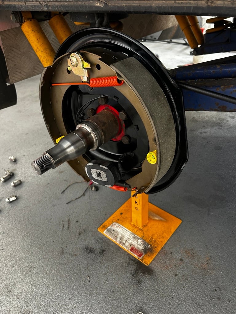 Automotive brake assembly mounted on yellow stand in workshop, showing rotor, caliper, and suspension components