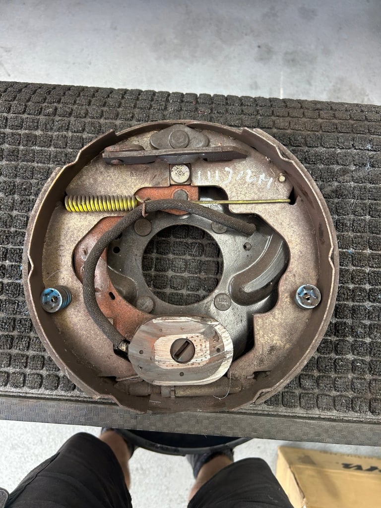 Internal view of a vehicle drum brake assembly showing metal components, springs, and mechanical parts on a textured surface