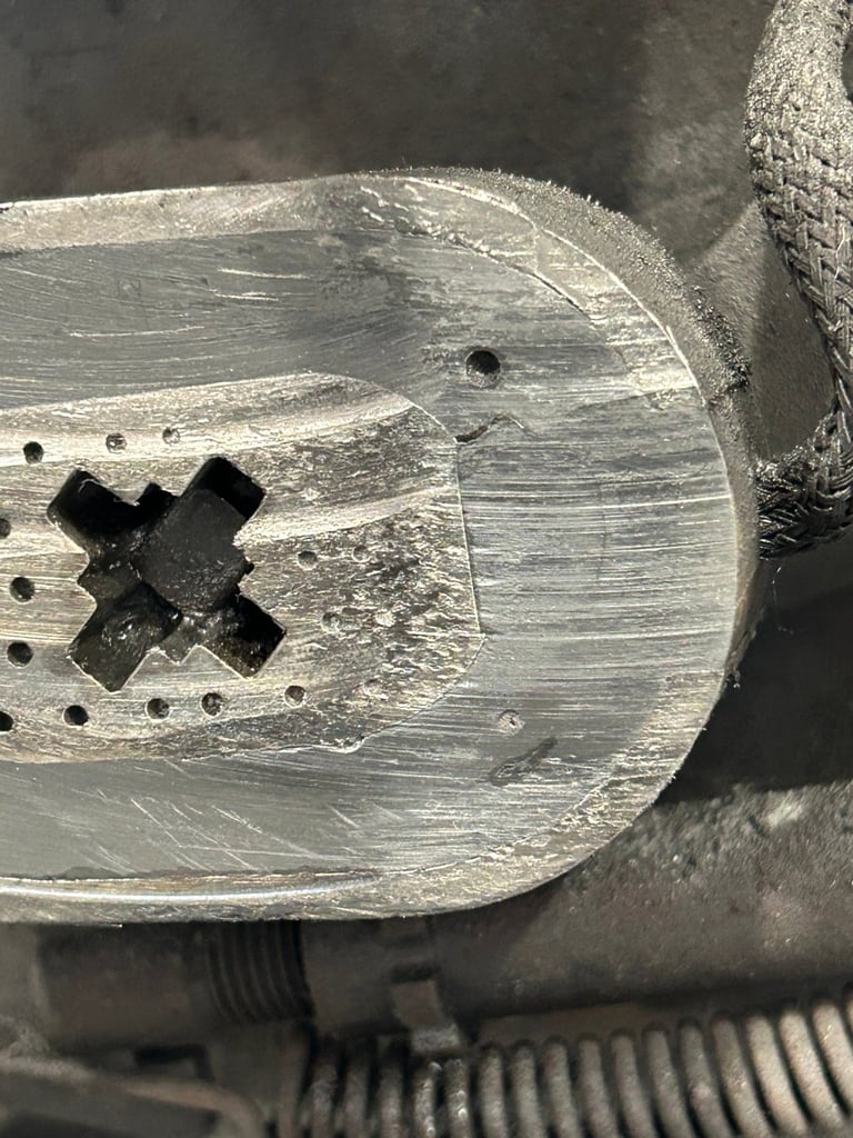Close-up of a weathered metal socket adapter with a cross-shaped attachment and mounting holes, covered in dust and wear marks