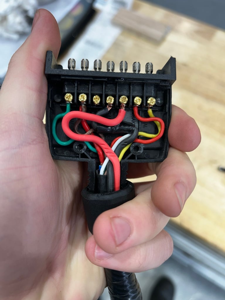 Close-up of a persons hand holding an electrical plug connector with brass terminals and colorful wires including red, yellow, green, and black
