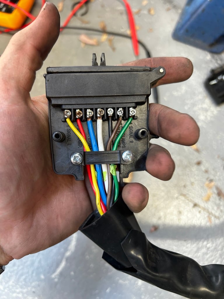 Hand holding a wiring connector with colorful wires (red, yellow, blue, white, green) attached to metal terminals and screws